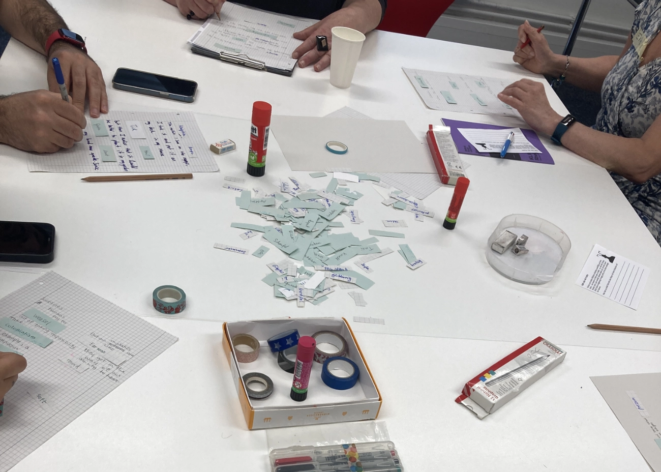 Materialien für kreative Schreibübung auf einem Tisch. Hände von Menschen, die Lückentexte ausfüllen.