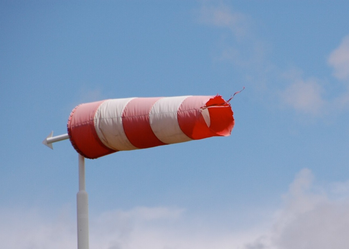 Das Bild zeigt einen Windsack, der senkrecht zum Pfosten im Wind weht